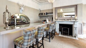 A bar area with a marble countertop, plaid barstools, a mounted deer head, and a fireplace. - The Alexandra Court Hotel (Congleton)