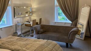A bedroom with a large bed, a chaise lounge, a vanity with a mirror, and a chandelier. - The Alexandra Court Hotel (Congleton)