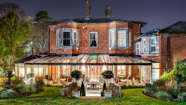 A large brick house with a glass conservatory, outdoor seating area, and a well-maintained garden. - The Alexandra Court Hotel (Congleton)