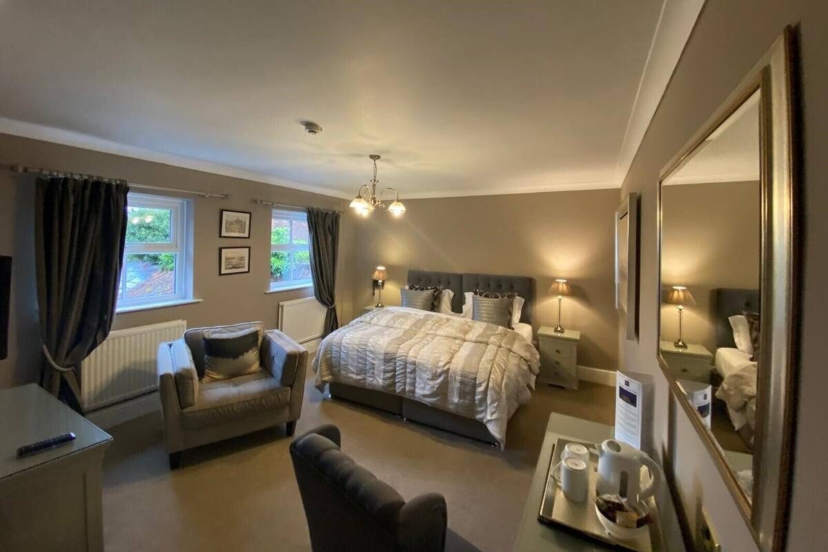 A bedroom with a bed, bedside tables, a chair, a dresser, a mirror, and a window with curtains.