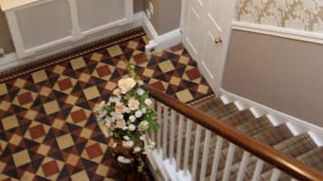 A staircase with a patterned floor, a chandelier, and a door with a floral wallpaper design.