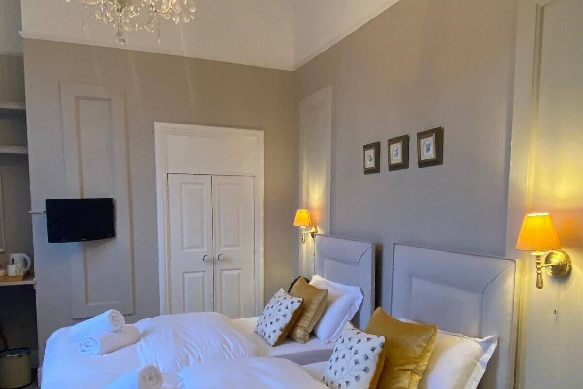 A hotel room with a large bed, a chandelier, two bedside lamps, a television, and a door.