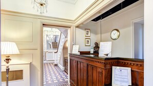A reception area with a check-in counter, a chandelier, a clock, and a patterned floor. - The Alexandra Court Hotel (Congleton)