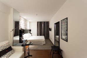 Habitación de hotel con cama, escritorio con silla, espejo y pared con inscripción decorativa.