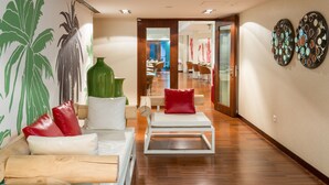 A modern hotel lobby with a wooden floor, a white sofa with red cushions, a green vase, and two wall art pieces. - Porto Trindade Hotel (Porto)