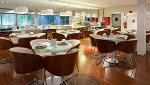 A modern dining area with round tables and brown chairs, featuring a buffet with various food items and a fire extinguisher on the wall. - Porto Trindade Hotel (Porto)