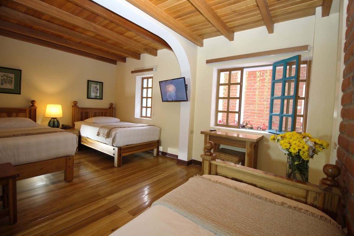 Una habitación con dos camas de madera, un televisor instalado en la pared y una ventana con persiana azul.