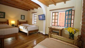 Una habitación con dos camas de madera, un televisor instalado en la pared y una ventana con persiana azul.