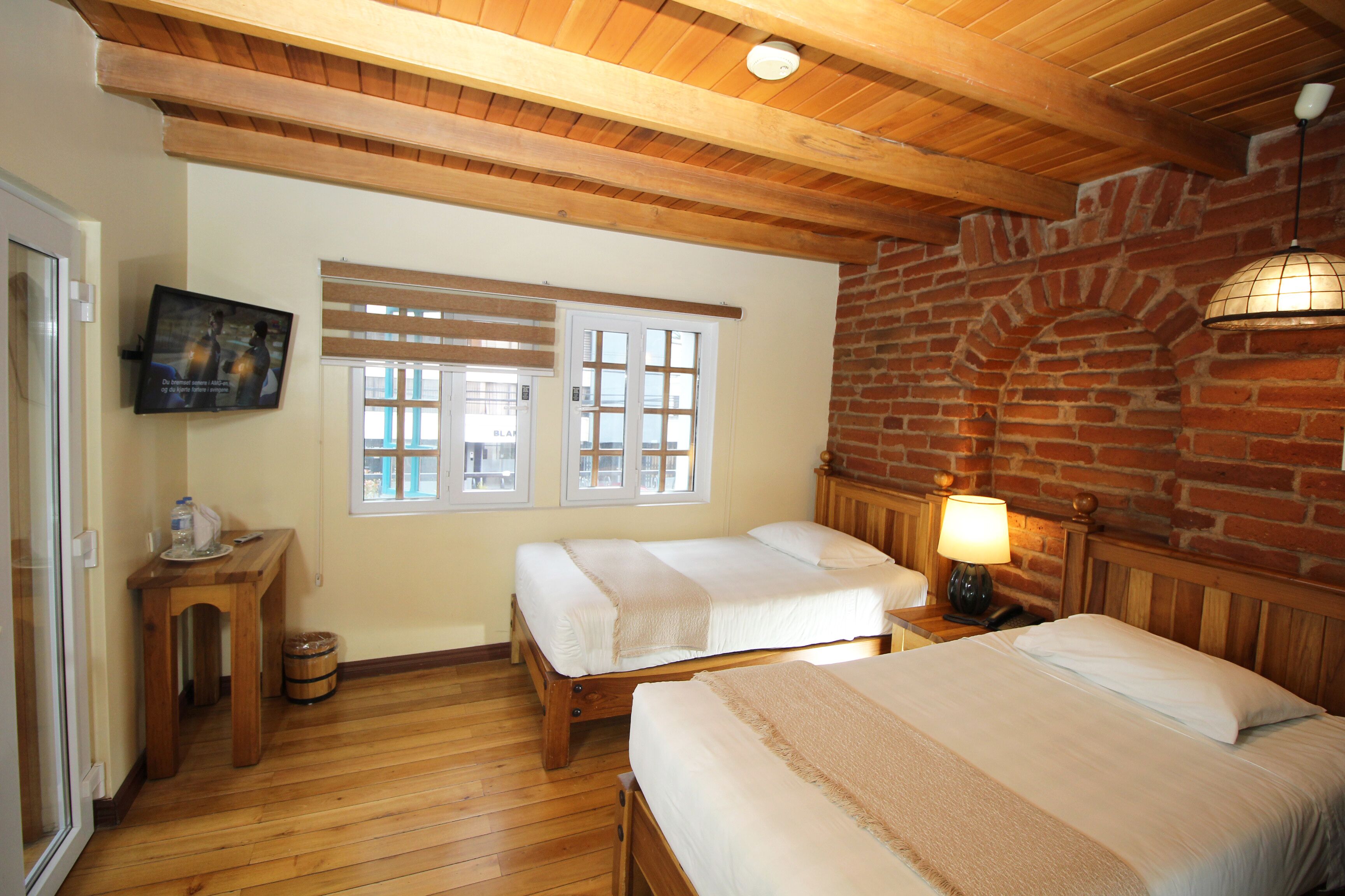 Une chambre avec deux lits, un plancher en bois, un téléviseur fixé au mur et un mur en briques.