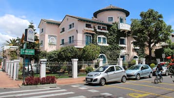 A building with a sign indicating it is in Cuba, a street with cars and a cyclist, and a crosswalk.