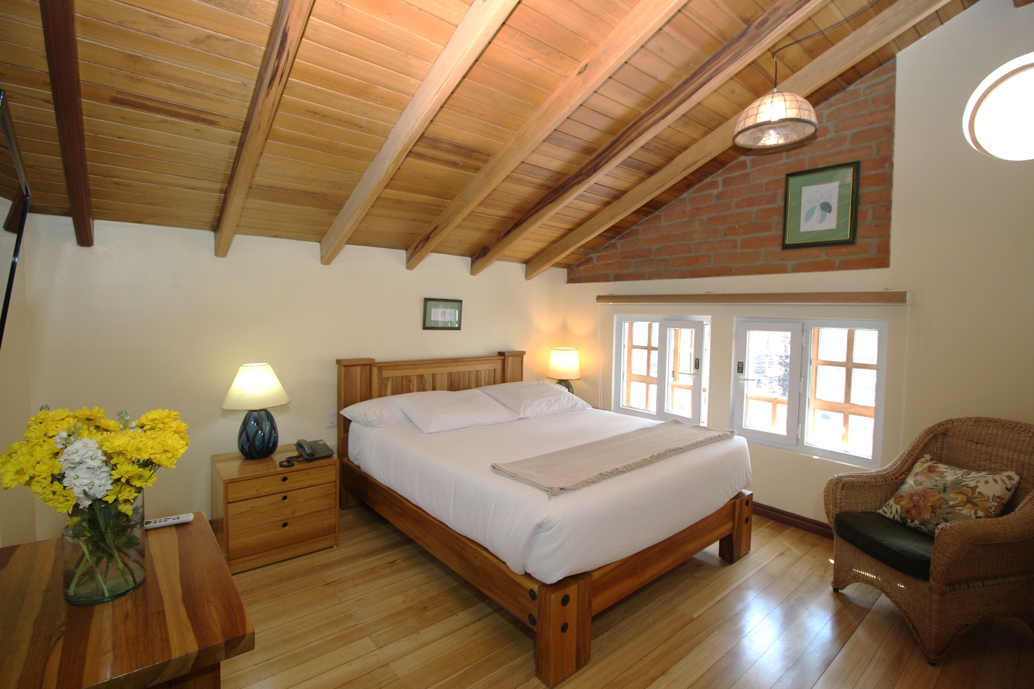 A bedroom with a wooden bed, bedside tables, a chair, and a window with a view.