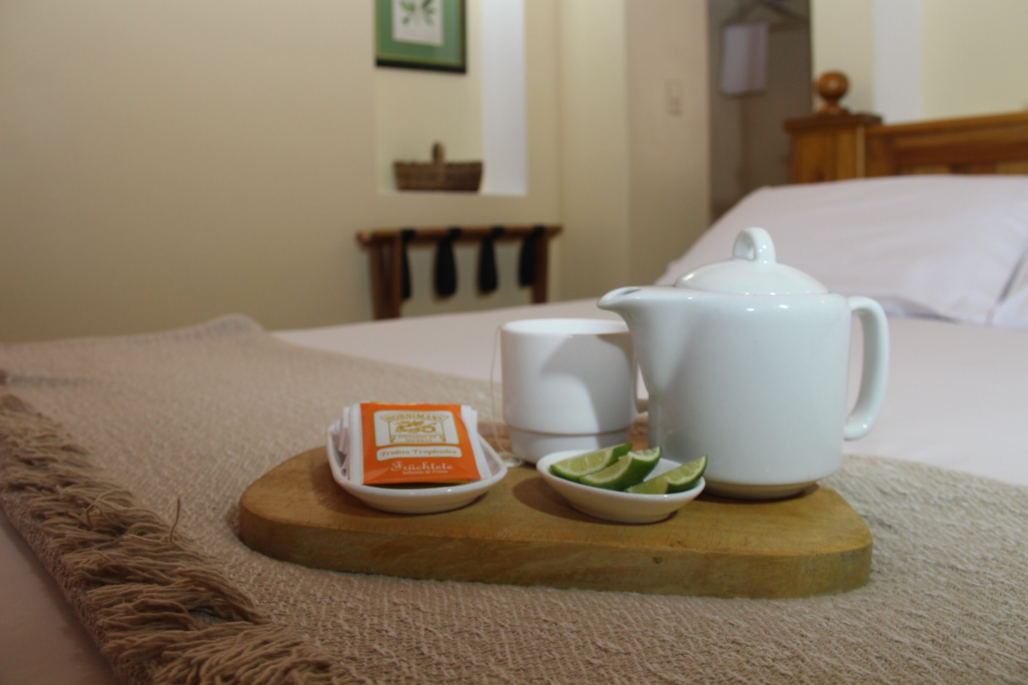 Una bandeja de madera con una tetera, una taza, un pequeño cuenco de rodajas de limón y un sobre de azúcar sobre una cama.