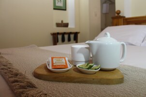 Una bandeja de madera con una tetera, una taza, un pequeño cuenco de rodajas de limón y un sobre de azúcar sobre una cama.