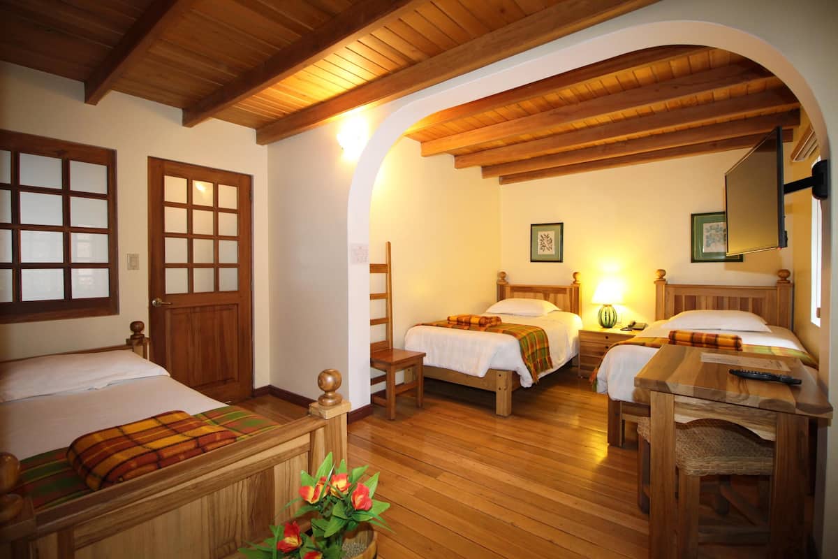 Una habitación con suelo de madera, dos camas, una silla de madera, una mesa y un espejo.
