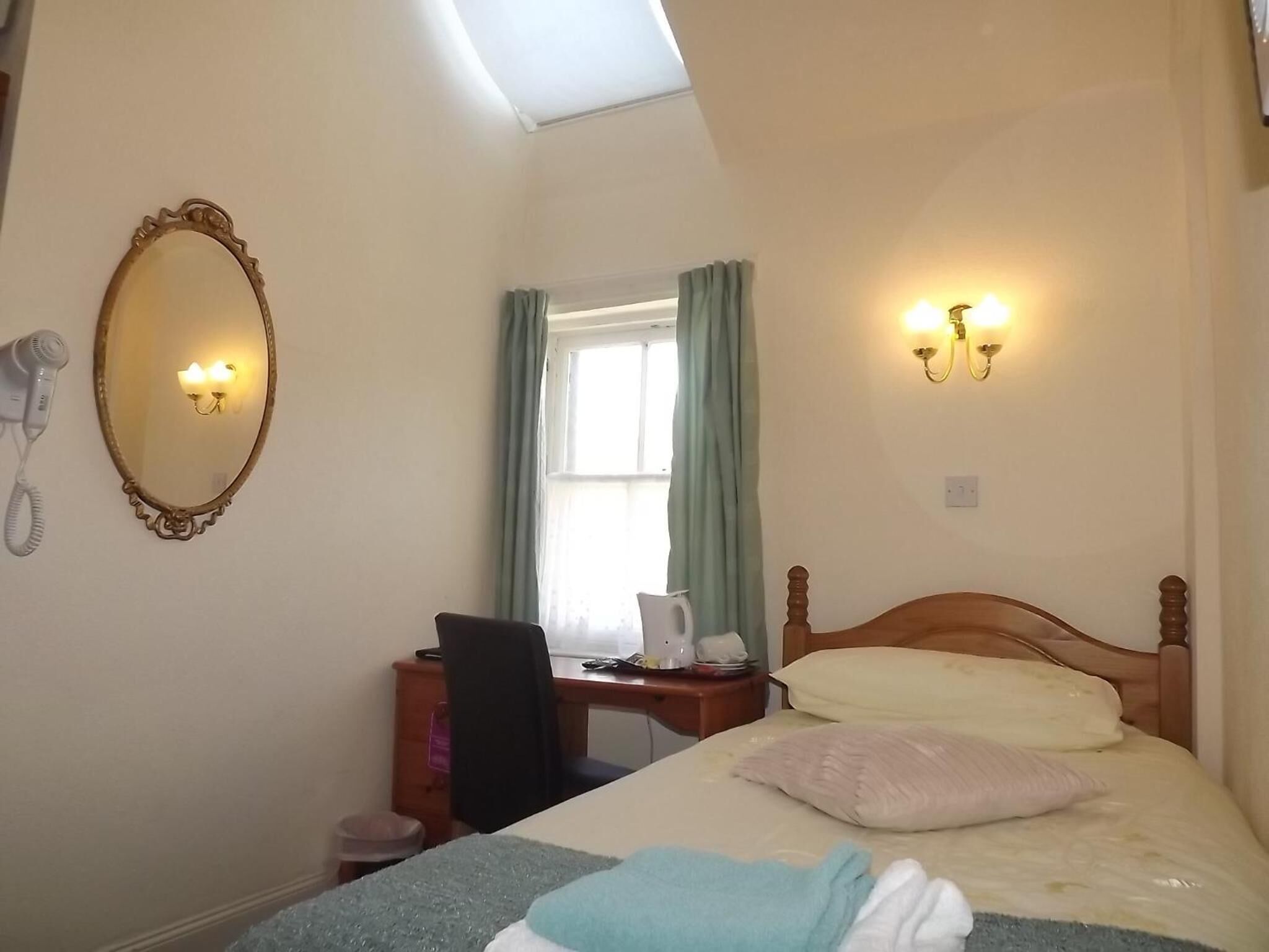 A hotel room with a bed, a desk, a chair, a mirror, a telephone, and a window with curtains.