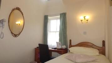 A hotel room with a bed, a desk, a chair, a mirror, a telephone, and a window with curtains.