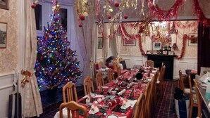 Une salle à manger décorée pour Noël, avec un sapin, des décorations rouges et dorées, et une longue table dressée pour le repas.