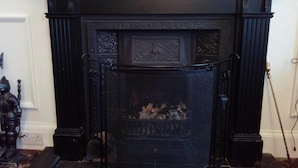 Une cheminée agrémentée d’un manteau décoratif et d’une porte-grille en métal.