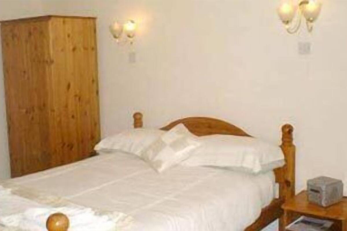 Quarto com cama de madeira, roupa de cama branca e duas luminárias fixadas na parede.