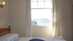 Une chambre à coucher avec un lit, des rideaux blancs et une vue sur une étendue d’eau et un paysage lointain.