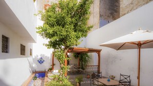 A courtyard with a tiled floor, a pergola, outdoor furniture, and potted plants.
