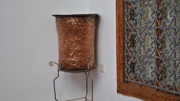 A copper pot on a metal stand against a wall with a decorative metal grille.