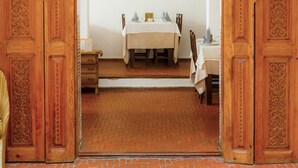 An interior view of a dining area with a table set for two, flanked by intricately carved wooden doors and an arched doorway.