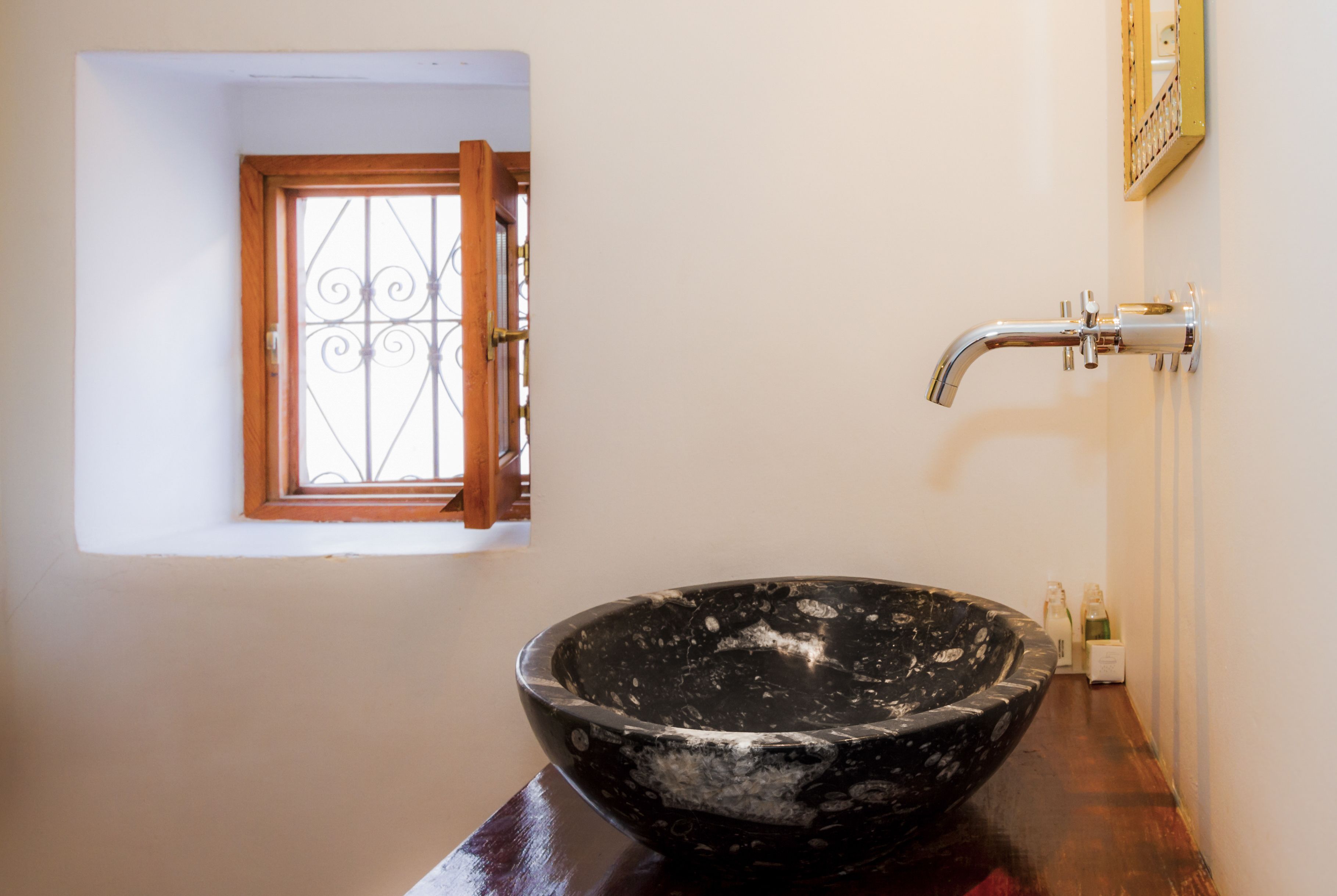 A bathroom with a black bowl sink, a window with a metal grill, and a wall-mounted faucet.