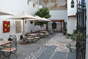 An outdoor patio with tables and chairs, umbrellas, and a tiled walkway.