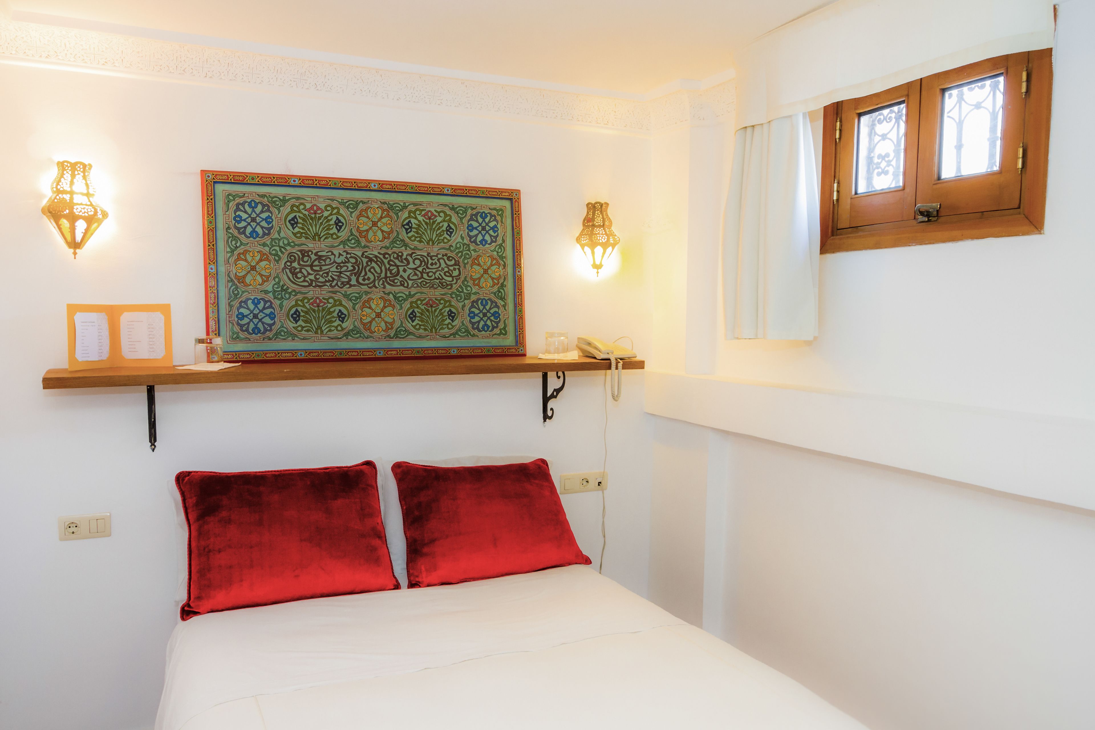 Ein Bett mit roten Kissen, einem Wandbehang und zwei Wandleuchten.