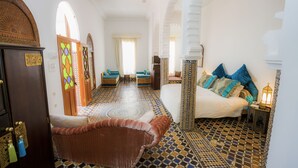 A room with a patterned floor, a bed with blue and white bedding, a brown sofa, and a wooden cabinet with a door.