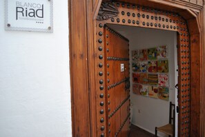 A wooden door with riveted edges, a sign for "BLANCO Riad hotel & restaurant", and colorful artwork on the wall.