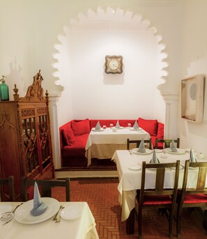 A dining area with a red sofa, white tables, and a clock on the wall.
