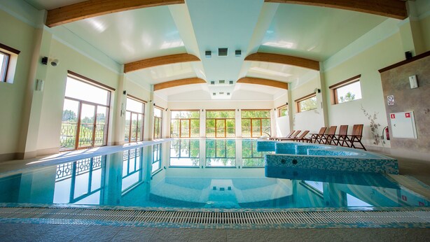 Ein großer, überdachter Pool mit Holzbalken, großen Fenstern und Fliesenböden.