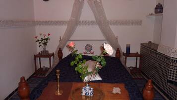 A traditional room with a bed, a table with a vase, and decorative items.