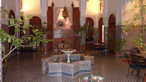 Un interior marroquí con una fuente, suelo de azulejos, arcos e iluminación cálida.