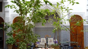 Un interior tradicional marroquí con suelo de mosaicos, puertas ornamentadas y una zona de estar central con mesa y sillas.