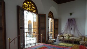 Un dormitorio con una cama grande, un sofá, un dosel y vistas al exterior a través de ventanas ornamentales.