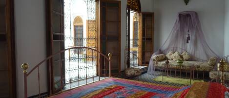 Une chambre à coucher avec un grand lit, un canapé, un baldaquin et une vue sur l’extérieur grâce à de magnifiques fenêtres.