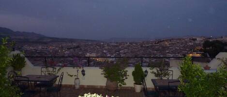 A rooftop terrace with outdoor seating and a view of a cityscape at dusk.