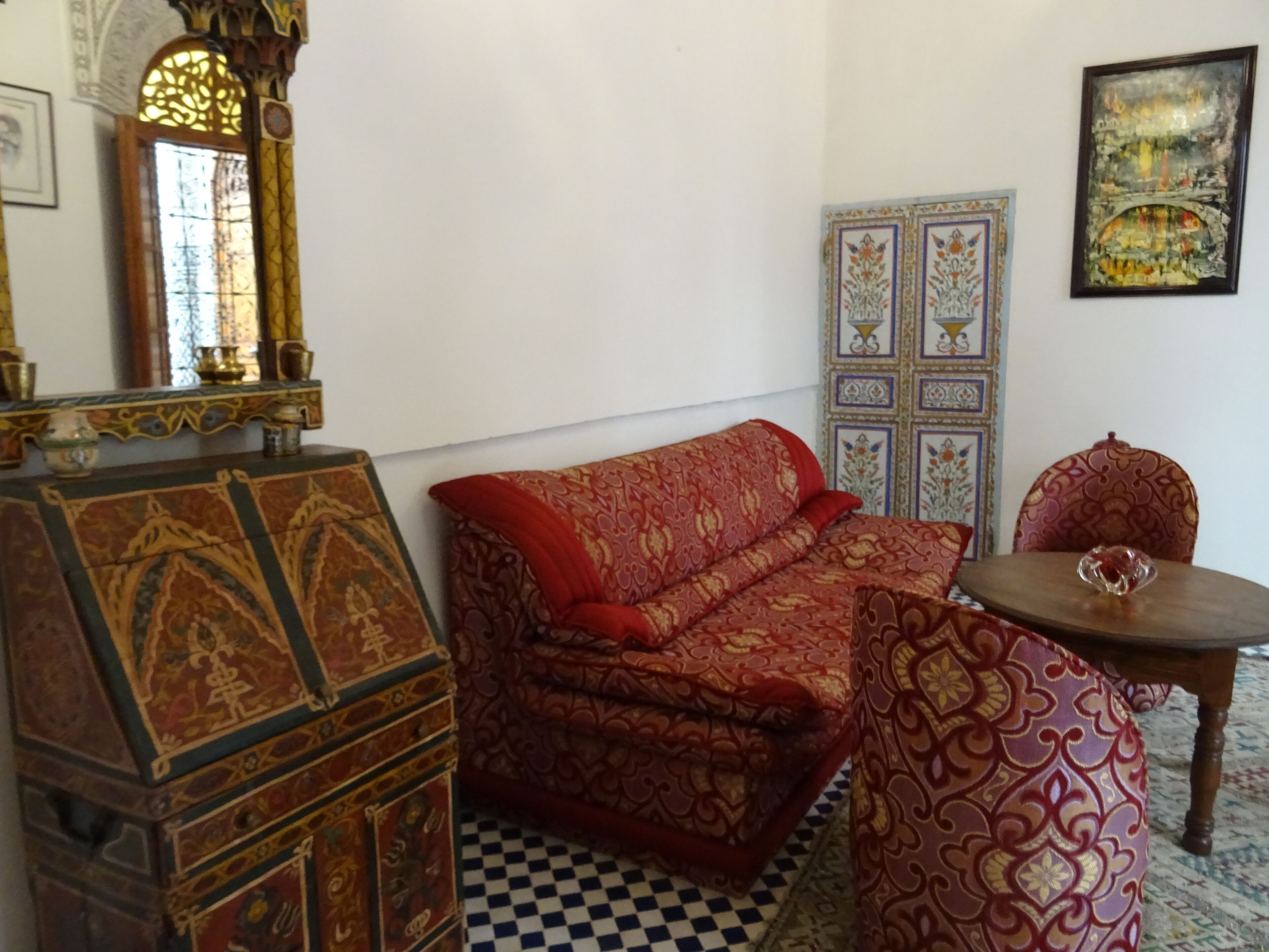 Una habitación con un sofá estampado, un aparador de madera, suelo a cuadros y un espejo decorativo.