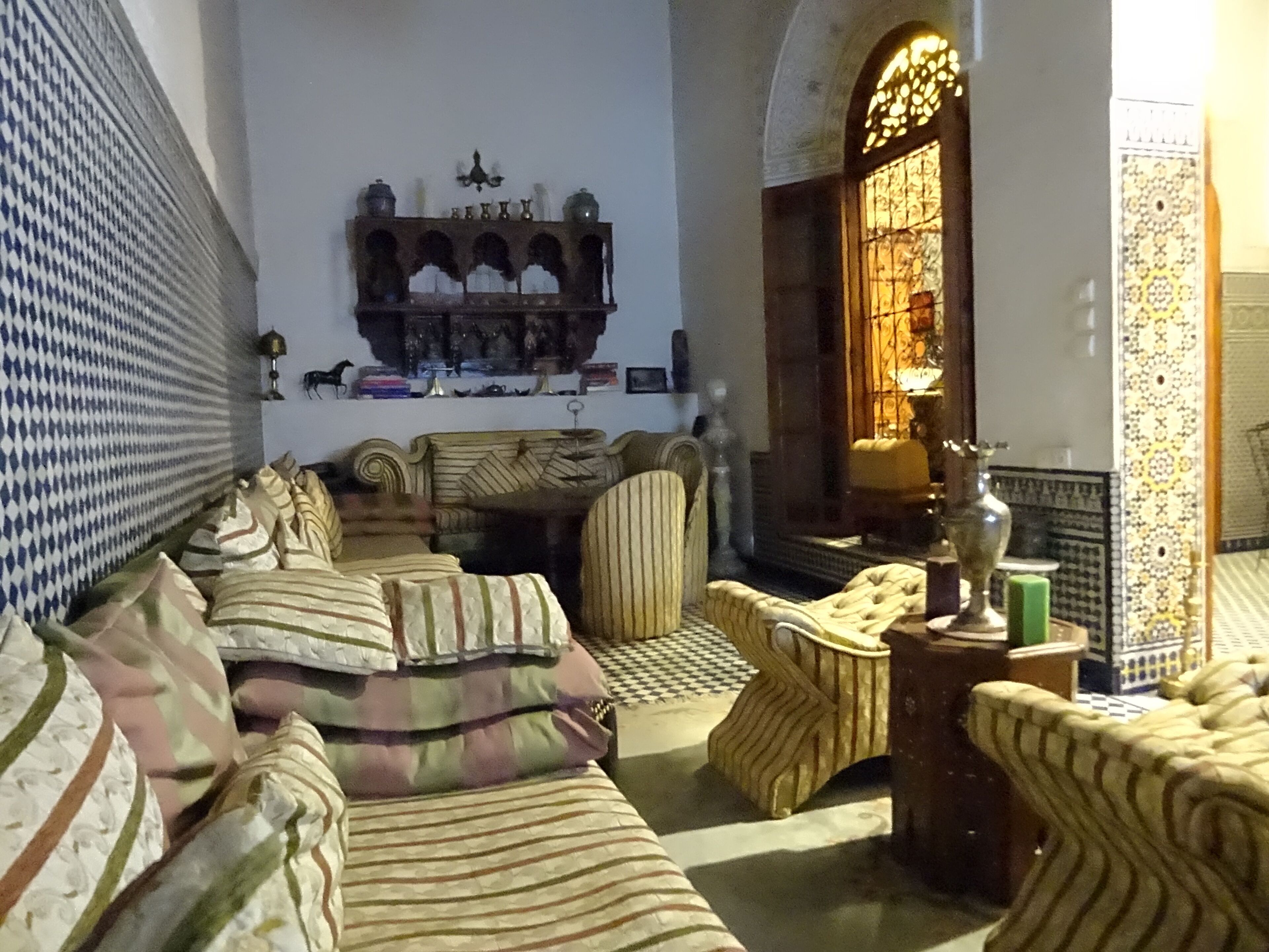 A cozy living room with a sofa set, a patterned rug, a decorative wall shelf, and a stained glass window.