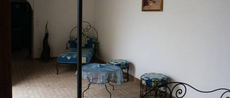 A room with a bed, a small table, and a chair. There is a painting on the wall and a window with curtains.