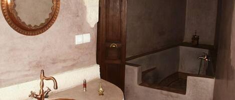 A bathroom with a copper sink, a wooden door, and a mirror on the wall.