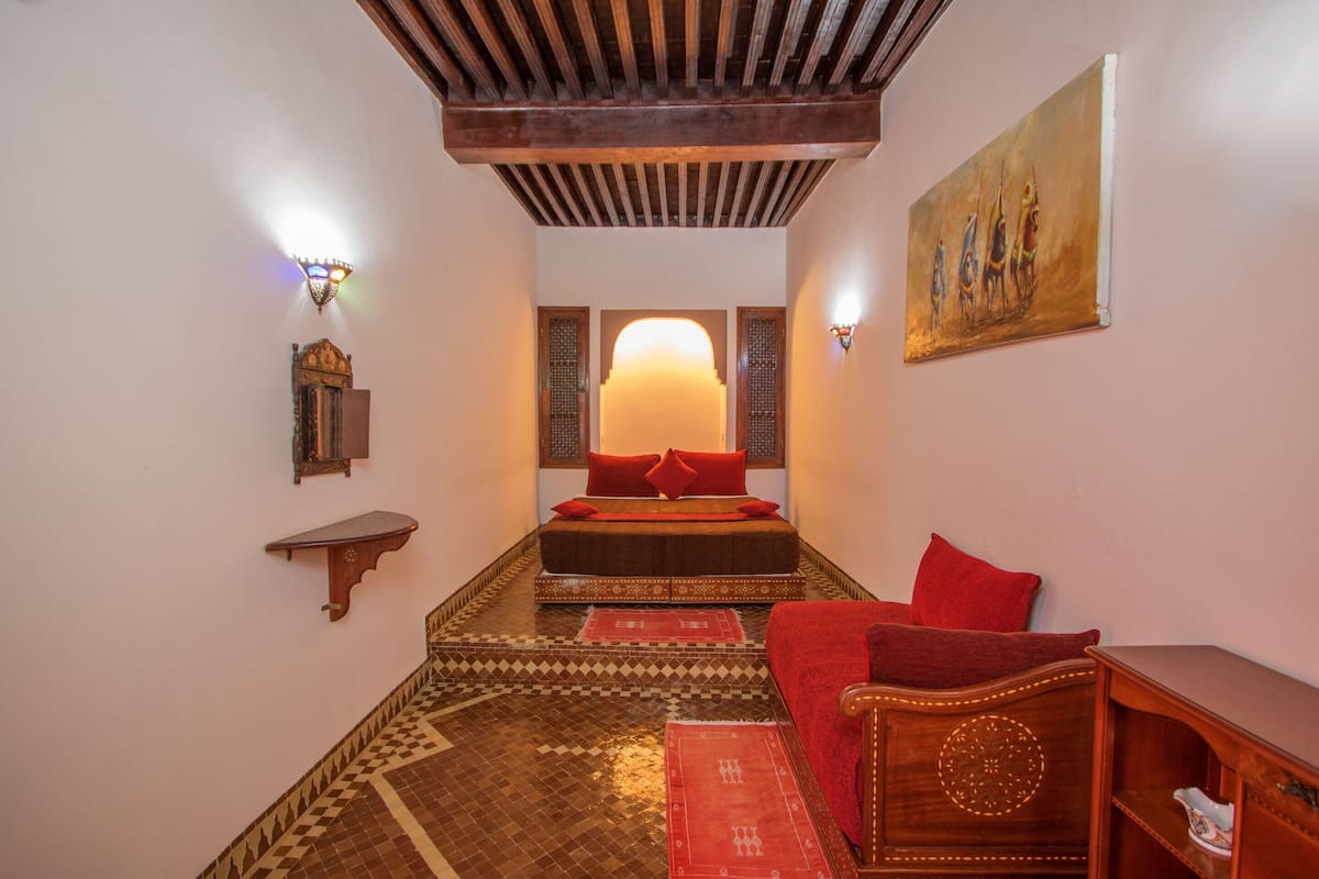 A room with a bed, a red sofa, a wooden cabinet, and a wall-mounted painting.