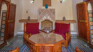 A traditional Moroccan interior with a wooden ceiling, a central fireplace, and patterned tile flooring. - Riad Zitouna (Fes)