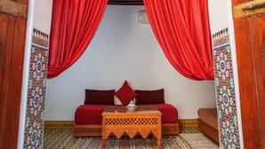 An ornate doorway with red curtains, a patterned floor, and a sofa with a matching cushion. - Riad Zitouna (Fes)