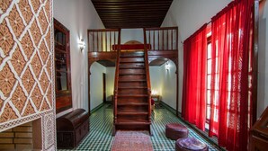 A staircase leading to a loft bedroom with a checkered floor, a red curtain, and a patterned rug. - Riad Zitouna (Fes)