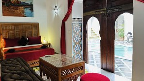 A room with a bed, a small table, a sofa, and a view of an outdoor pool area. - Riad Zitouna (Fes)