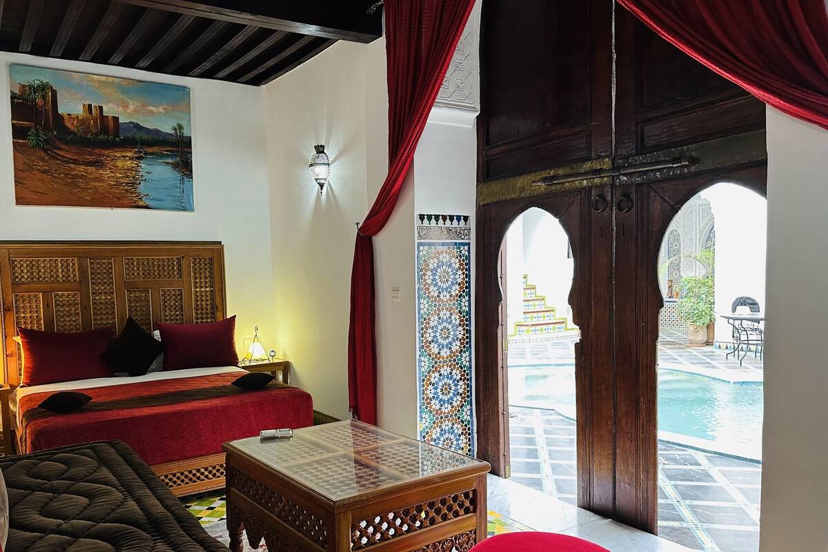 A room with a bed, a small table, a sofa, and a view of an outdoor pool area.